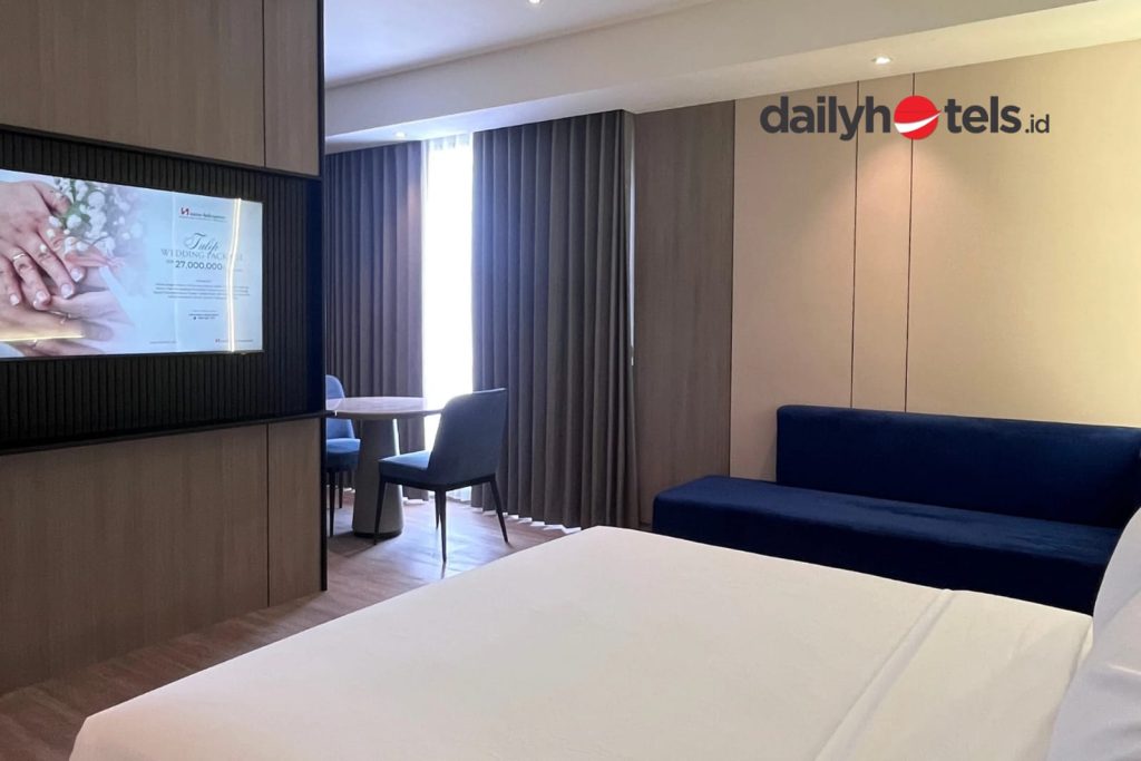 A spacious Express Suite hotel room with a large premium bed, a separate seating area or sofa, modern minimalist furniture, and elegant interior decor at Swiss-Belexpress Jemursari Surabaya.