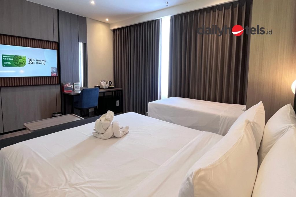 A large, modern hotel room designed for families, featuring multiple beds or a combination of a king bed and twin beds, clean white linens, and functional wooden furniture at Swiss-Belexpress Jemursari Surabaya.