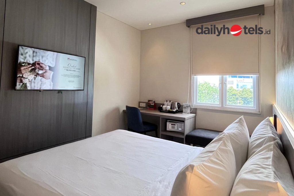 Interior of an Express Super Room featuring a larger bed with white linens, contemporary wooden furniture, a work desk, and warm interior lighting at Swiss-Belexpress Jemursari Surabaya.