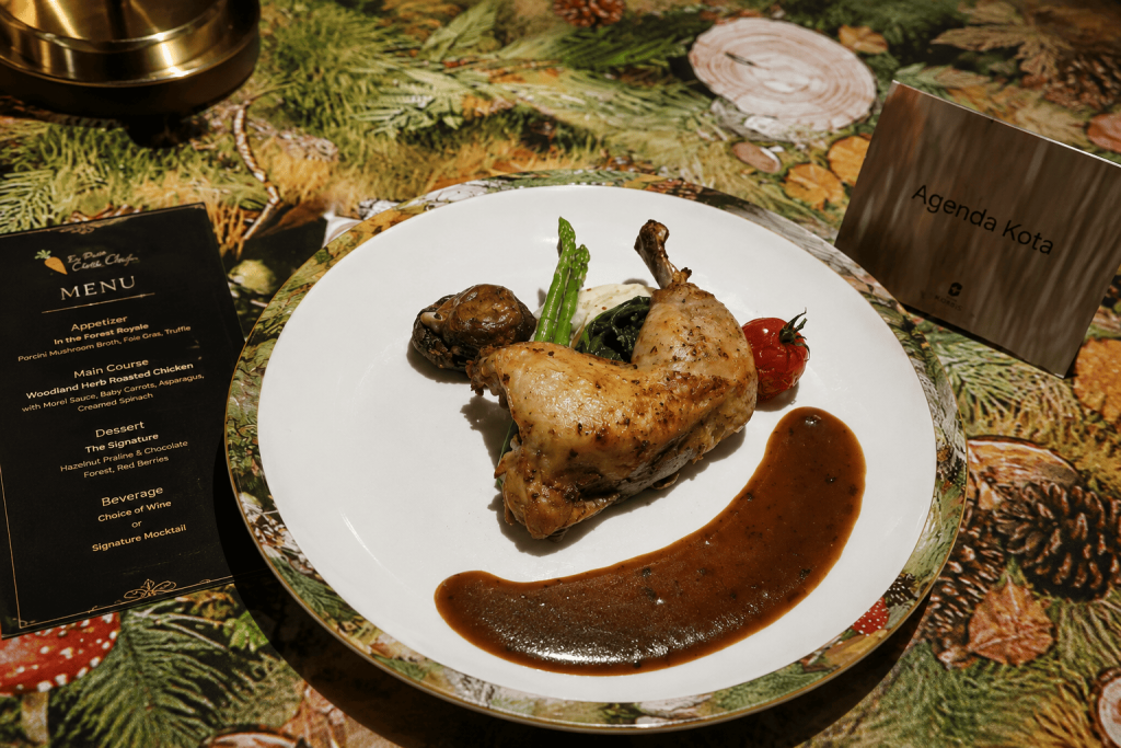 Foto hidangan ayam panggang dengan asparagus, jamur, sayuran hijau, tomat ceri, dan saus cokelat yang disajikan di atas piring putih dalam pengalaman dining Le Petit Chef