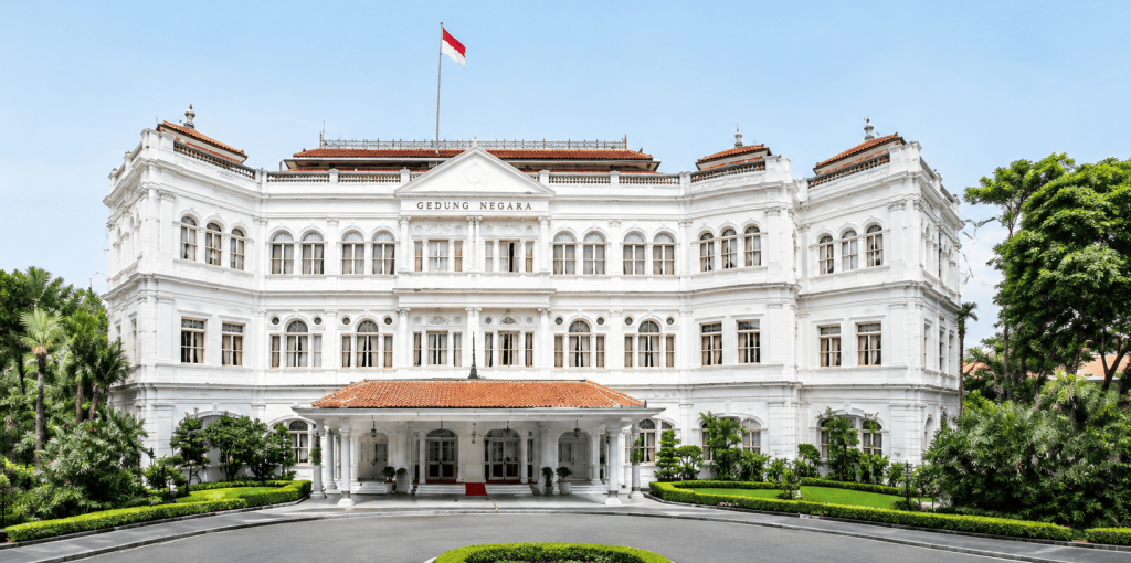 Raffles Singapore dengan arsitektur kolonial klasik dan taman hijau di bagian depan hotel