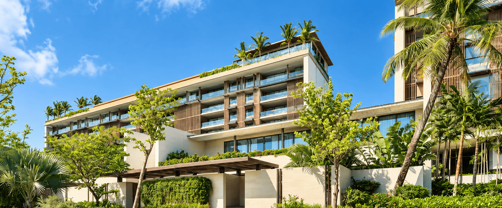 Regent Phu Quoc, resor mewah tropis dengan bangunan modern, balkon berlapis kaca, taman hijau, dan pohon palem di bawah langit biru.
