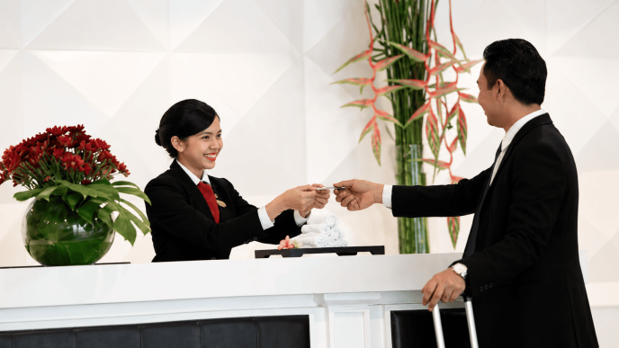Proses check-in hotel saat staf Front Office menyerahkan kartu kamar kepada tamu
