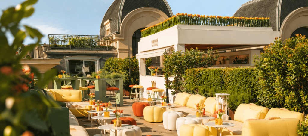 Area rooftop The Golden Hour di The Peninsula Paris dengan sofa bernuansa krem dan kuning, tanaman rambat, serta suasana outdoor yang elegan
