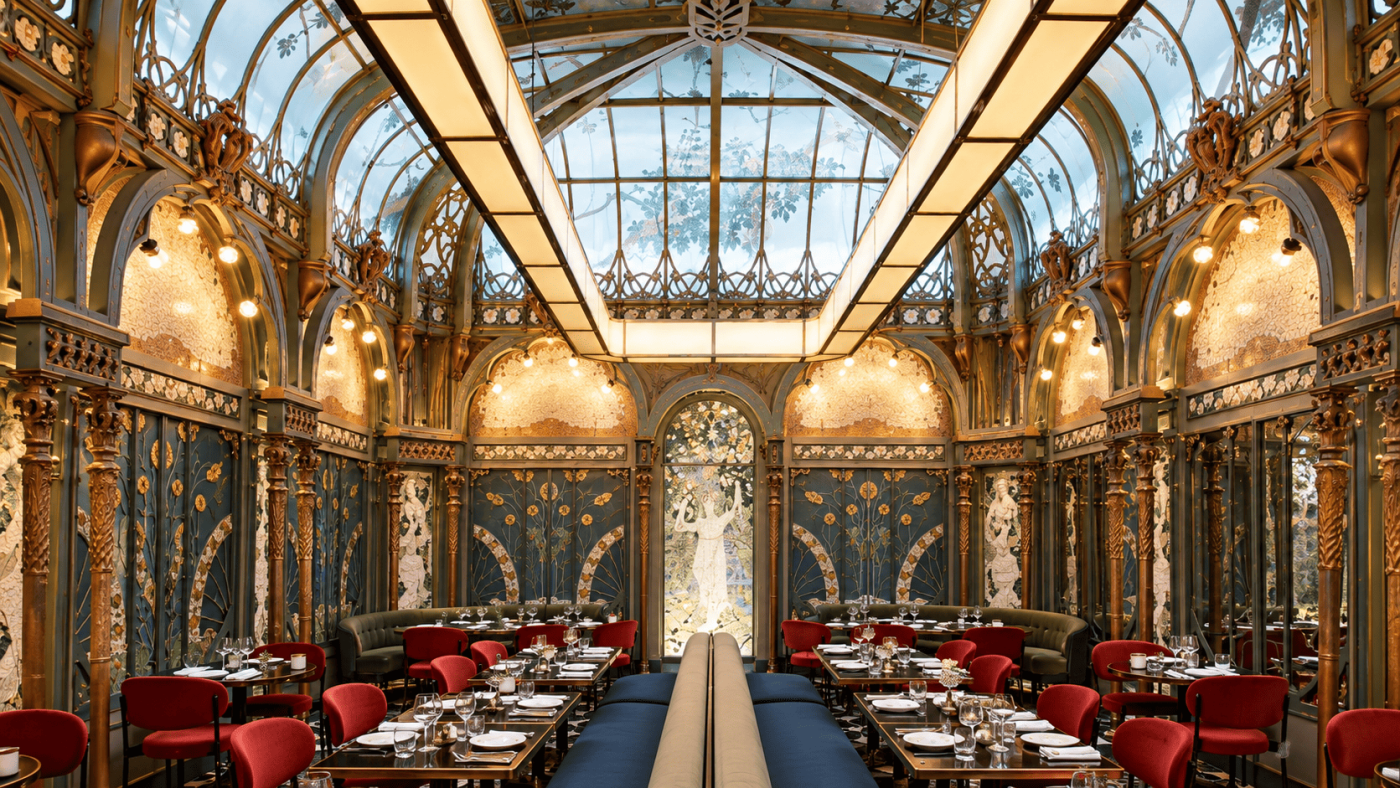 Interior Beefbar Paris dengan atrium kaca, dekorasi Art Nouveau, ornamen artistik, dan kursi makan berwarna merah