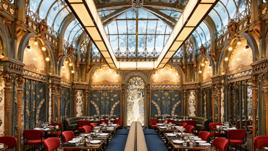 Interior Beefbar Paris dengan atrium kaca, dekorasi Art Nouveau, ornamen artistik, dan kursi makan berwarna merah