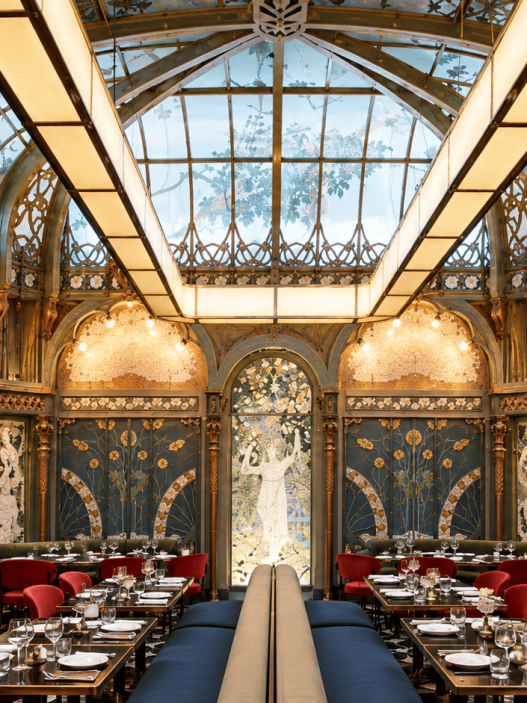 Interior Beefbar Paris dengan atrium kaca, dekorasi Art Nouveau, ornamen artistik, dan kursi makan berwarna merah