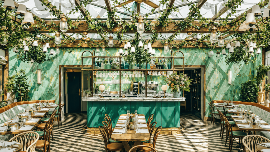 Interior restoran Pink Mamma di Paris dengan bar berwarna hijau, tanaman rambat, atap kaca, dan dekorasi bergaya Italia