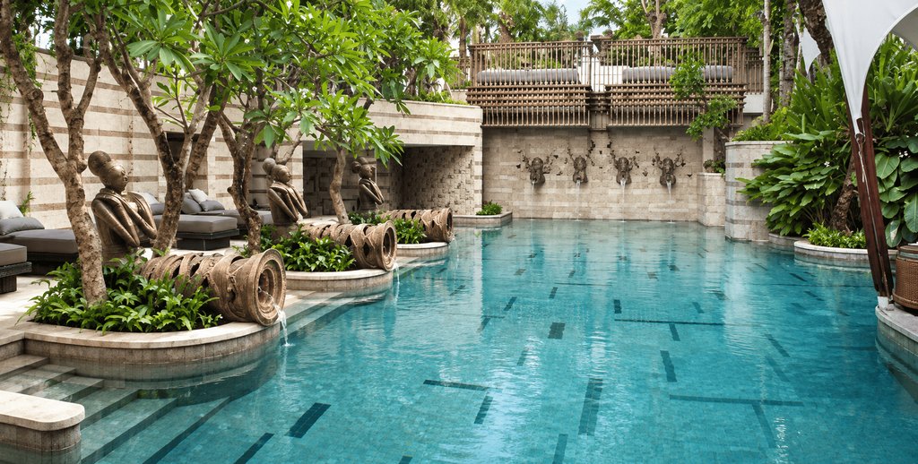 Kolam renang The St. Regis Jakarta dengan desain tropis, patung dekoratif, air mancur, dan area lounge yang dikelilingi pepohonan hijau.