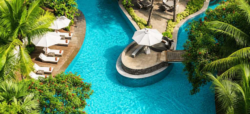 Kolam renang tropis DoubleTree by Hilton Jakarta – Diponegoro dengan area lounge, payung putih, dan pepohonan hijau.