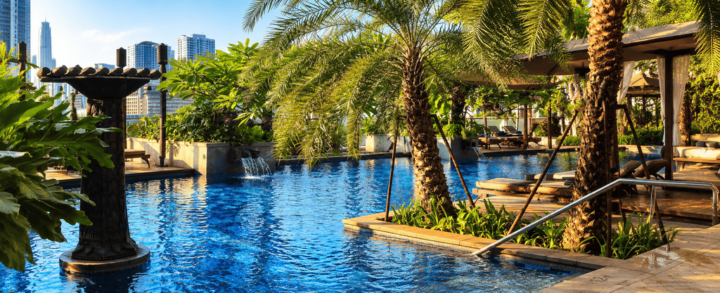 Kolam renang Four Seasons Hotel Jakarta dengan air biru, pepohonan tropis, area lounge, dan gedung-gedung.