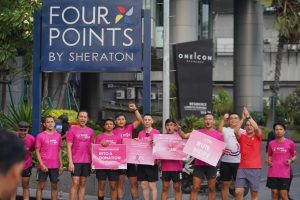 Peserta Road to Give 2026 berfoto bersama sambil membawa papan kampanye kepedulian kanker payudara di depan Four Points by Sheraton Surabaya