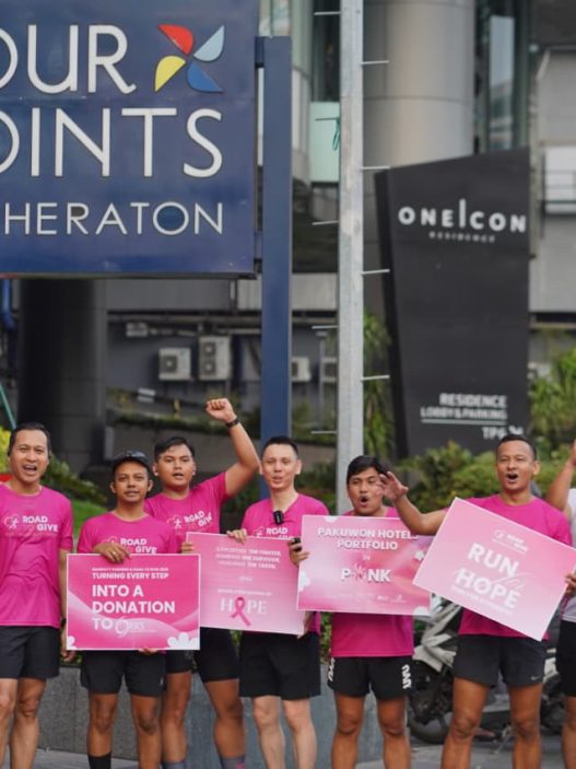 Peserta Road to Give 2026 berfoto bersama sambil membawa papan kampanye kepedulian kanker payudara di depan Four Points by Sheraton Surabaya