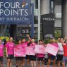 Peserta Road to Give 2026 berfoto bersama sambil membawa papan kampanye kepedulian kanker payudara di depan Four Points by Sheraton Surabaya